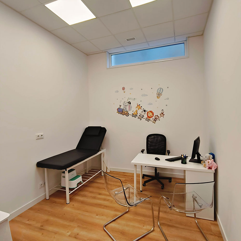 Consulta pediátrica luminosa en clínica sanitaria con camilla de exploración, escritorio médico y decoración infantil.