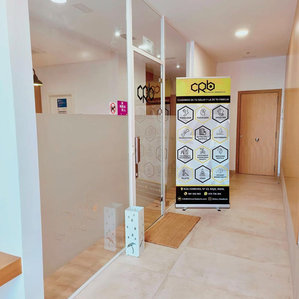 Acceso interior a Clínica Ribadavia en Noia, con puerta acristalada y panel informativo de especialidades médicas